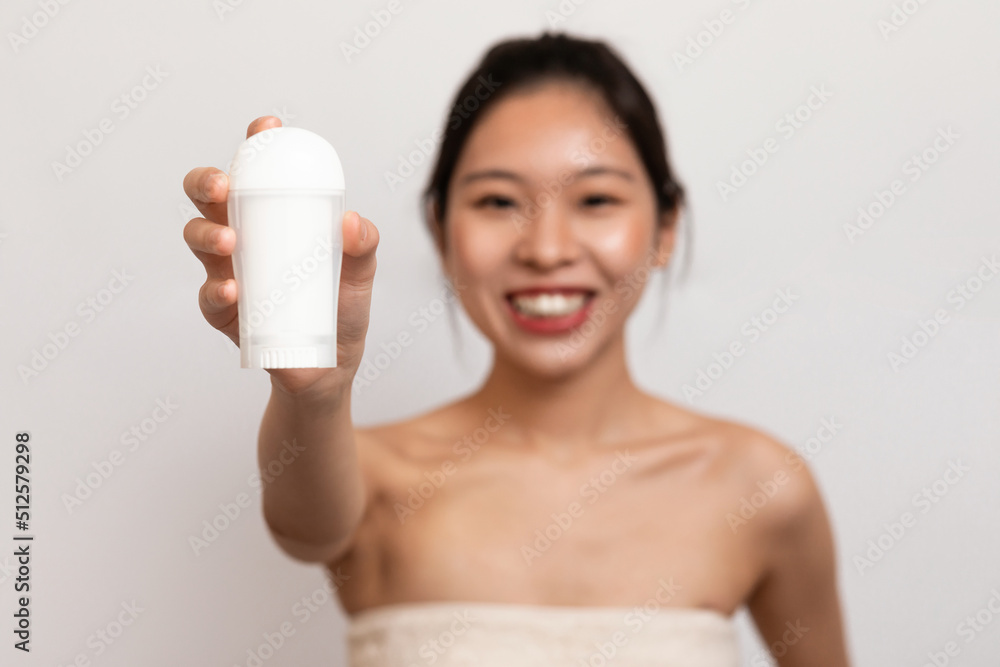 Personal hygiene and treatment after shower. Happy young asian lady in towel showing deodorant for armpit Personal hygiene and treatment after shower. Happy young asian lady in towel showing deodorant for armpit