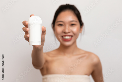 Personal hygiene and treatment after shower. Happy young asian lady in towel showing deodorant for armpit