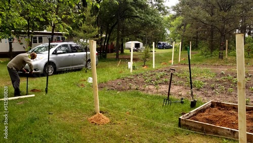 Man manual drill post hole for fence around vegetable garden to keep animals away. photo