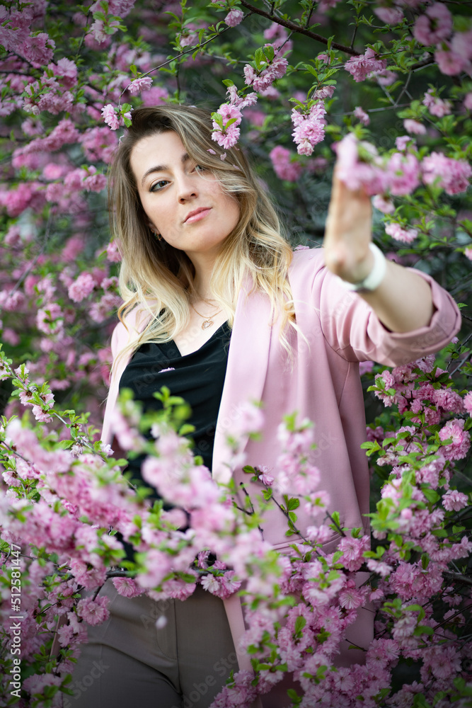 A very beautiful blonde in a pink jacket and a black blouse sensually poses standing among the flowers of cherry blossoms. Goddess of nature or earth A very beautiful blonde in a pink jacket and a black blouse sensually poses standing among the flowers of cherry blossoms. Goddess of nature or earth