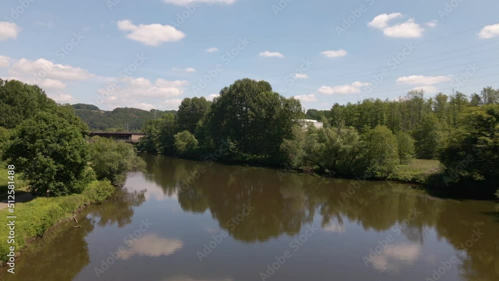 Blue sky and lush trees reflecting in the brown water of a calm river in west Germany. Wide angle aerial flyover Blue sky and lush trees reflecting in the brown water of a calm river in west Germany. Wide angle aerial flyover