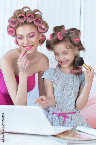 Mother and little daughter with hair curlers applying make up