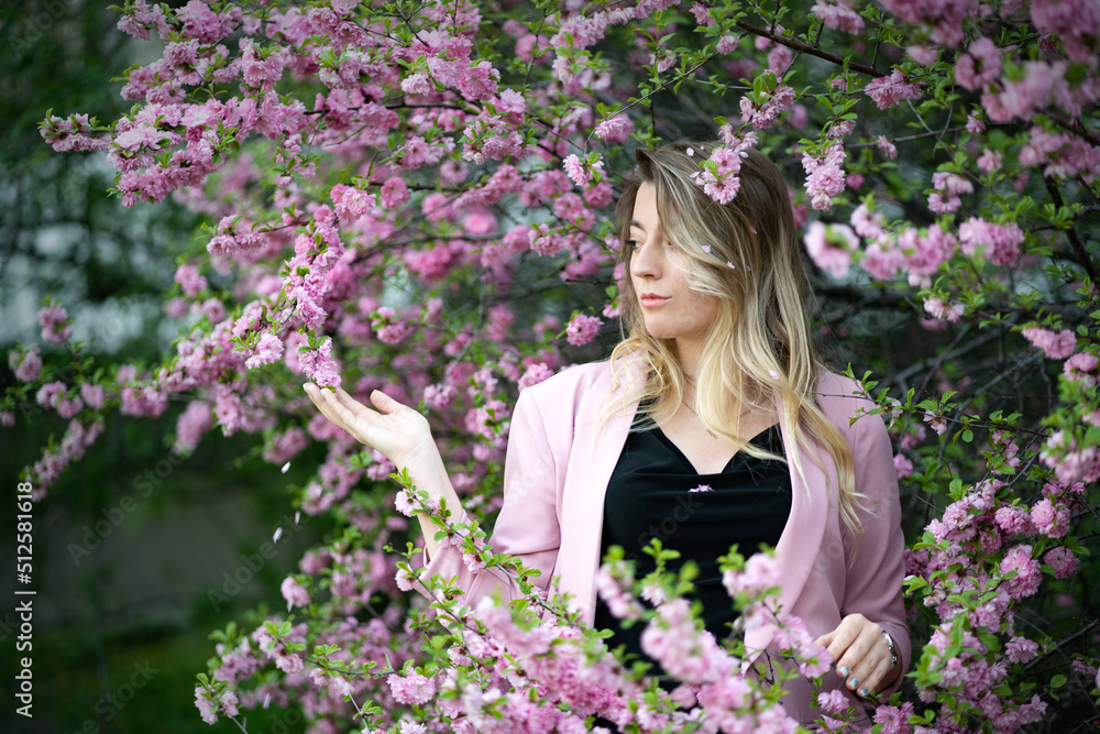 A very beautiful blonde in a pink jacket and a black blouse sensually poses standing among the flowers of cherry blossoms A very beautiful blonde in a pink jacket and a black blouse sensually poses standing among the flowers of cherry blossoms