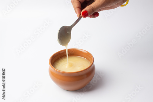 Pure cow ghee in ceramic bowl on white background with ghee spoon in hand