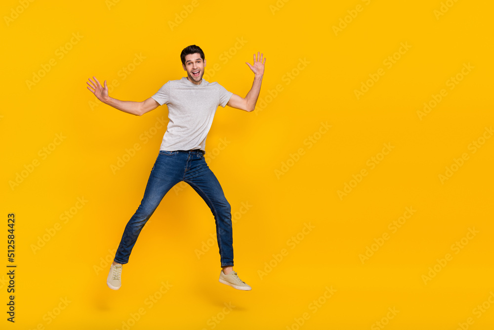 Full size photo of cool brunet young guy run jump wear t-shirt jeans footwear isolated on yellow background