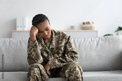 Depression Concept. Portrait Of Upset Black Female Soldier Sitting On Couch Indoors © Prostock-studio