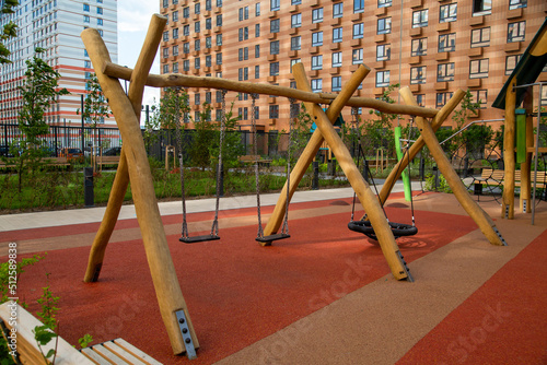 Fotografie Swing assembled from the trunks of yellow trees on the playground in the courtyard of the house outdoors