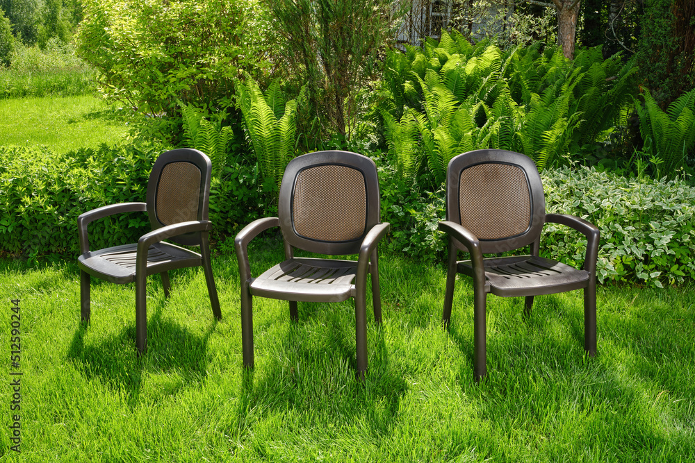 Fototapeta premium Chairs in the garden. Plastic chairs in ornamental garden background. Selective focus.