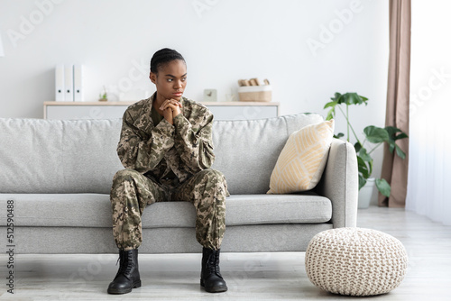 Pensive black soldier woman in military uniform with ptsd sitting on couch © Prostock-studio