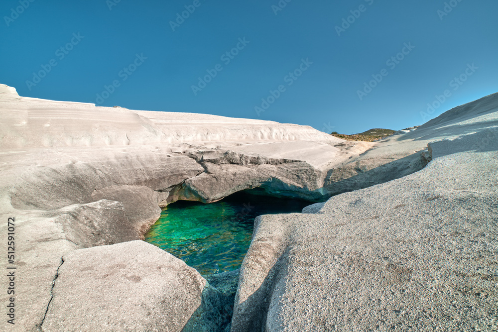 Unique white rocks and emerald green water in sea cave, Sarakiniko beach, Milos island, Greece. Empty cliffs, summer sunshine, clear blue sky