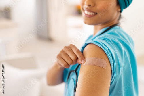 Midsection of smiling biracial young female doctor showing bandage on arm at clinic photo