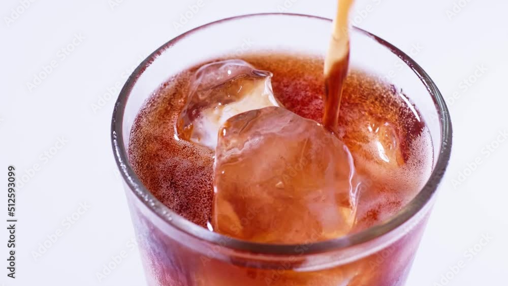 Coca Cola is poured into a glass from a bottle. White background Coca Cola is poured into a glass from a bottle. White background