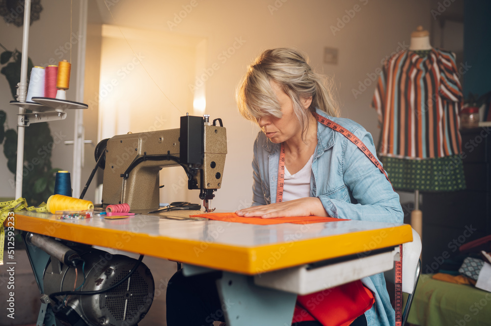 Tailor woman sitting and sewing on a sewing machine a in studio Tailor woman sitting and sewing on a sewing machine a in studio
