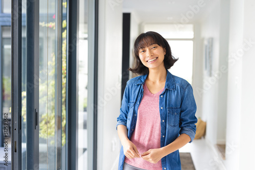 Portrait of smiling asian young woman with short hair wearing denim jacket standing by window photo