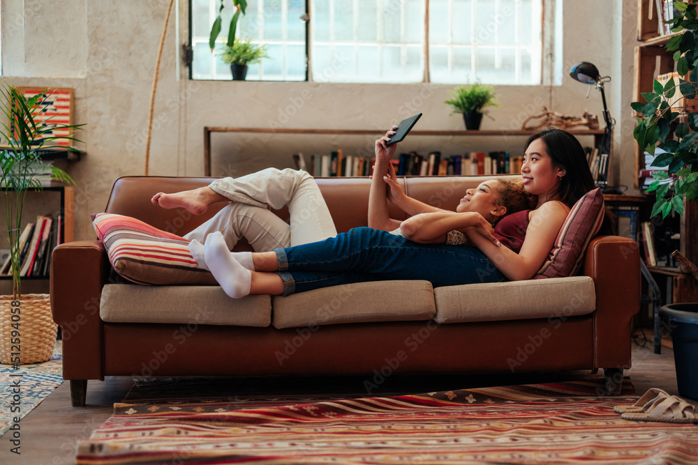 Lesbian couple lying on couch using tablet