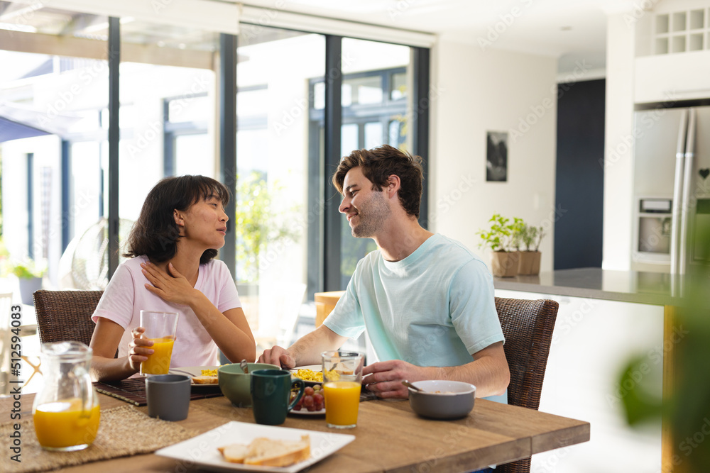 Smiling multiracial young couple talking while having breakfast at dining table in morning Smiling multiracial young couple talking while having breakfast at dining table in morning