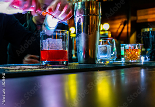 bartender hand making negroni cocktail. Negroni classic cocktail and gin short drink with sweet vermouth, red bitter liqueur and dried orange garnish.