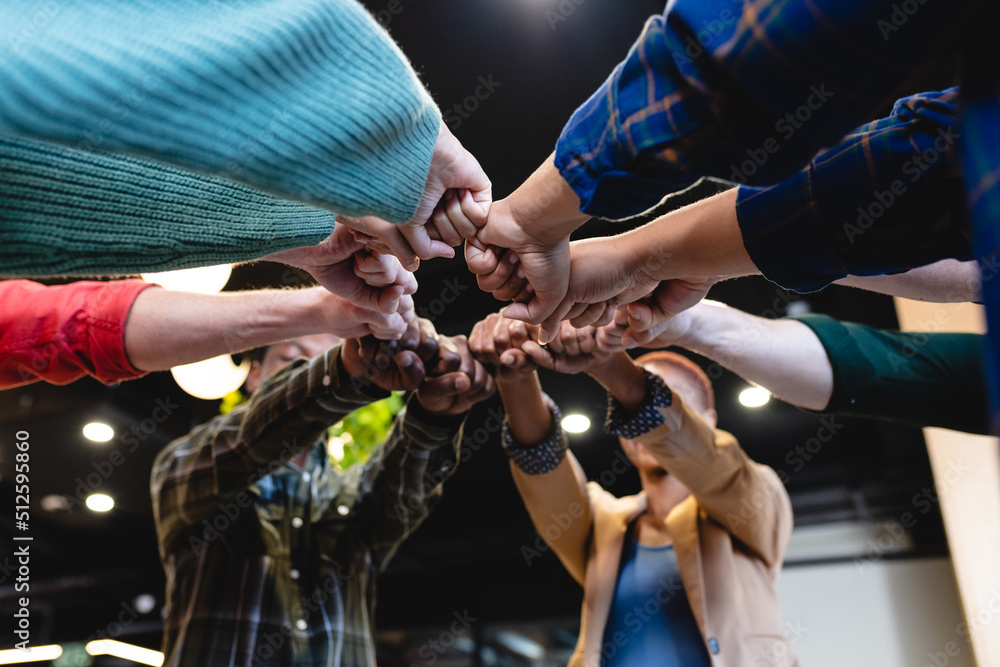 Multiracial fashion designers huddling with clenched fists in office Multiracial fashion designers huddling with clenched fists in office