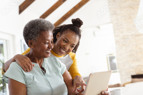 Smiling african american young daughter pointing at laptop being used by senior mother on table photo