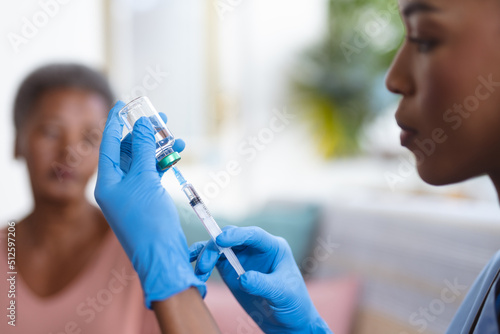 African american senior woman looking at young female doctor holding vial and syringe at home photo