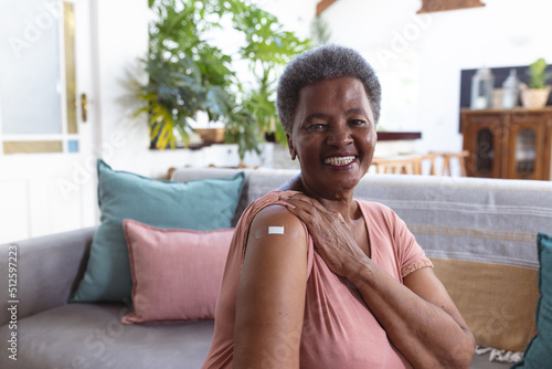 Portrait of smiling african american senior woman with adhesive bandage on shoulder sitting on sofa photo