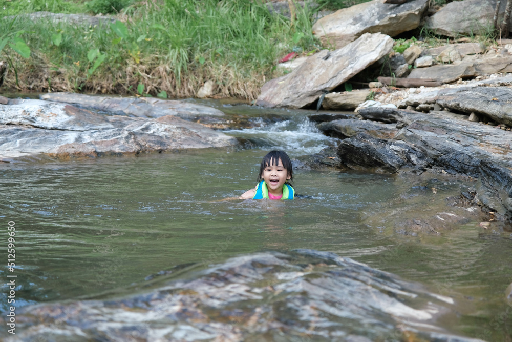 Little girls enjoy swimming in the river. Cute Asian girl wearing a life jacket is having fun playing in the stream. Healthy Summer Activities for Kids. Little girls enjoy swimming in the river. Cute Asian girl wearing a life jacket is having fun playing in the stream. Healthy Summer Activities for Kids.
