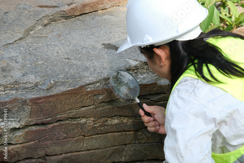 Asian female geologist researcher analyzing rocks with a magnifying glass in a natural park. Exploration Geologist in the Field. Stone and ecology concept. photo