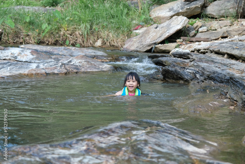 Little girls enjoy swimming in the river. Cute Asian girl wearing a life jacket is having fun playing in the stream. Healthy Summer Activities for Kids.