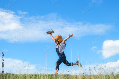 Cute little girl running through the meadow on a sunny day with a toy plane in hand. Happy kid playing with cardboard plane against blue summer sky background. Childhood dream imagination concept. photo