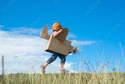 Фотография Cute dreamer little girl playing with cardboard planes in the meadow on a sunny day
