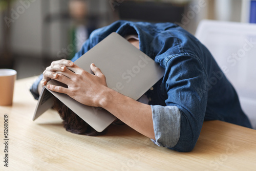 Depressed Young Man Sitting At Desk And Covering His Head With Laptop photo