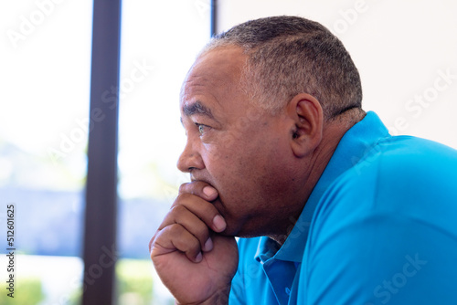 Side view of thoughtful biracial senior man with hand on chin looking away in retirement home
