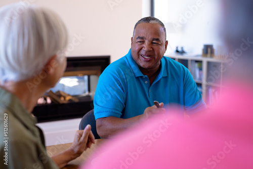 Smiling biracial senior man talking with asian friend while having breakfast in retirement home