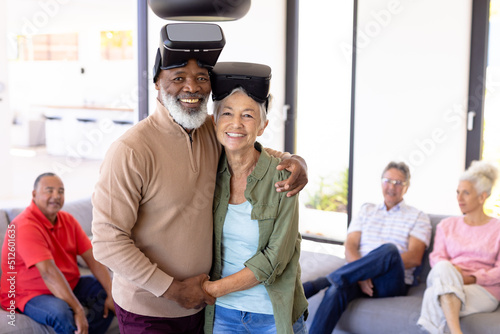 Portrait of happy multiracial senior friends wearing virtual reality simulators in retirement home