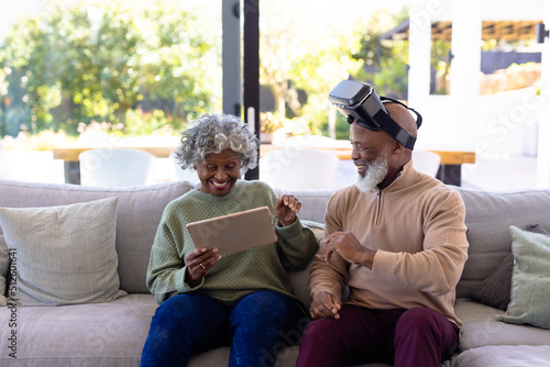 Cheerful african american senior friends using virtual reality simulator and digital pc on sofa