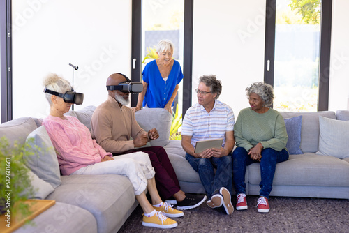 Multiracial seniors with digital pc looking at friends using virtual reality simulator on sofa