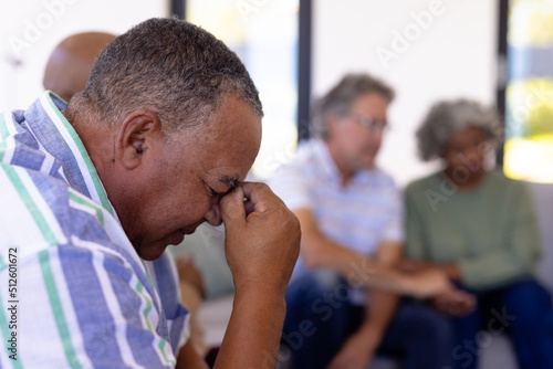 Close-up of depressed caucasian senior man with head in hand sitting with multiracial friends