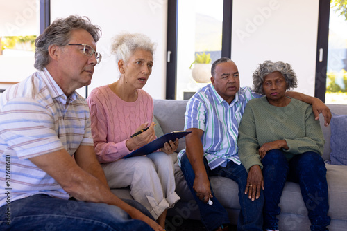 Multiracial female therapist sitting with seniors on sofa in therapy session at retirement home