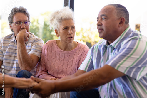Multiracial seniors looking at man holding woman's hands and comforting her in group therapy session