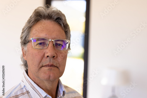 Close-up portrait of confident caucasian senior man wearing eyeglasses against wall in nursing home
