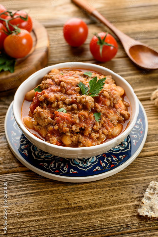 chili con carne with tomatoes and herbs on a wooden table, next to a spoon and vegetables chili con carne with tomatoes and herbs on a wooden table, next to a spoon and vegetables