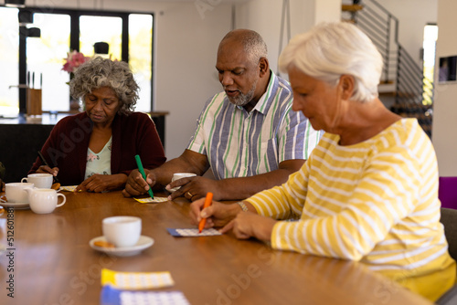 Multiracial senior friends with coffee cups on dining table playing bingo in nursing home