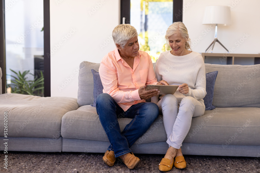 Biracial senior man showing digital tablet to smiling woman while sitting on sofa in nursing home Biracial senior man showing digital tablet to smiling woman while sitting on sofa in nursing home