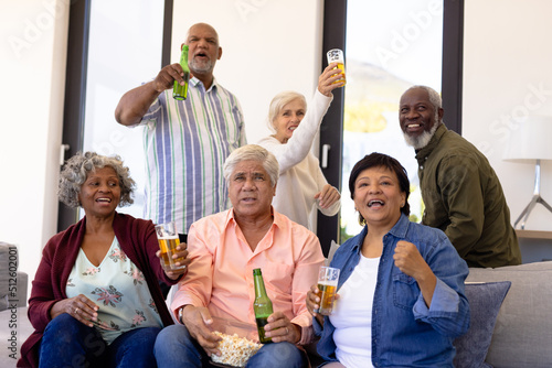 Multiracial excited senior friends with beer and popcorns enjoying match in nursing home
