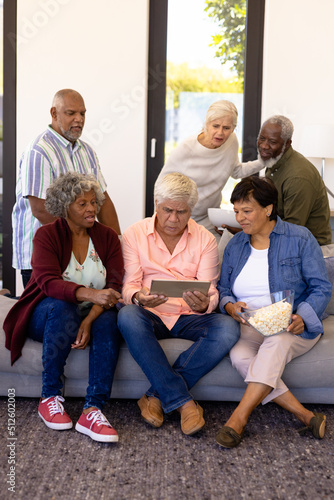 Multiracial senior friends with popcorns watching match over digital tablet in nursing home