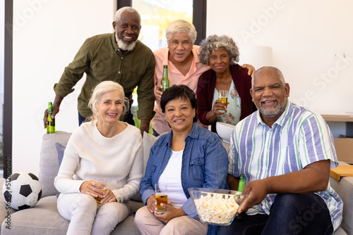 Portrait of cheerful multiracial senior friends with beer and popcorn enjoying match in nursing home