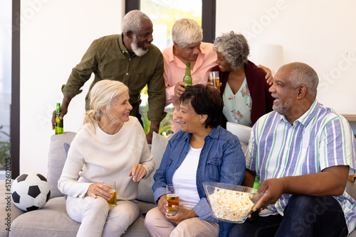 Cheerful multiracial senior friends talking while enjoying beer and popcorn in nursing home
