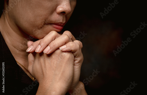 Close up of woman praying for christian religion with blurred black background.