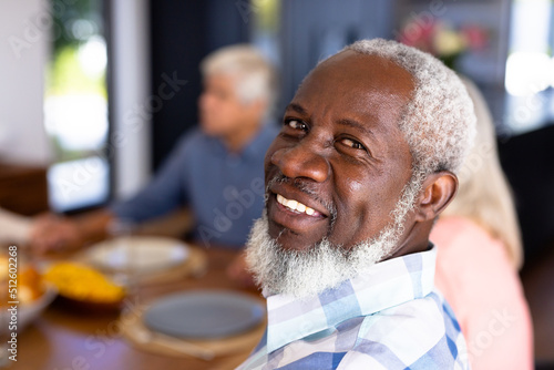Close-up portrait of african american senior man with multiracial friends sitting at dining table