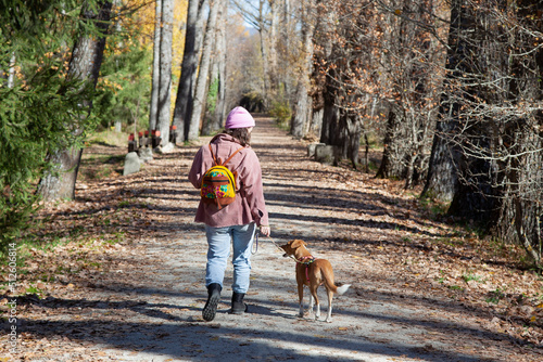 Mujer paseando por el sendero de un bosque junto a su perro. Chica de excursión con su mascota photo